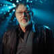 Actor Jonathan Frakes stands on a dimly-lit set, illuminated from behind by beams of light.
